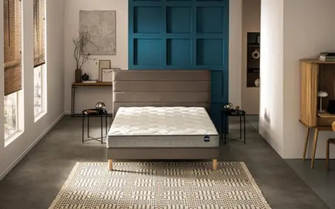 Un lit moderne avec un matelas blanc et un sommier gris, sur un tapis géométrique. Le prix moyen d'un bon matelas est un investissement pour le confort.