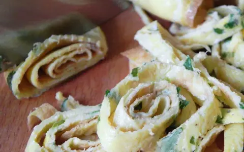 Roladki z jajek, idealne jako makaron keto z jajek, posypane szczypiorkiem, krojoną na desce.