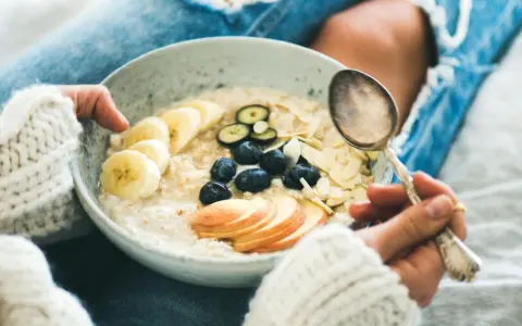 Schüssel mit Haferflocken, Bananen, Blaubeeren und Mandelsplittern. Ein Löffel wartet darauf, die gesunde Mahlzeit zu genießen, die nicht dick machen muss.