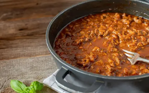 Un saporito ragù di anatra, ricetta veneta, pronto in padella con una forchetta. Profumo di basilico fresco.