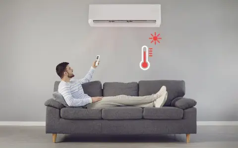 Hombre en sofá con control remoto ajustando el aire acondicionado calefacción. Termómetro rojo indica alta temperatura.