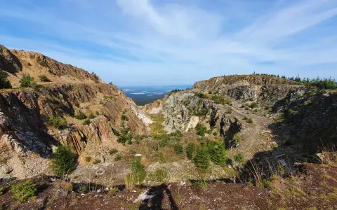 Krajobraz po wydobyciu w kopalni kwarcu Stanisław. Skarpy skalne, zarośla i niebo.