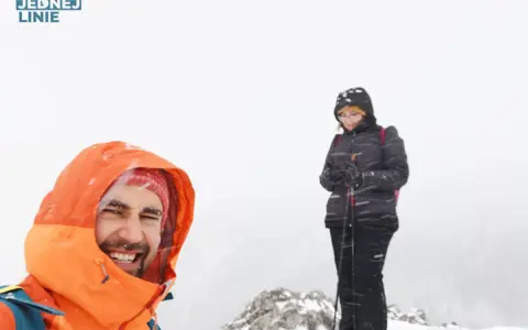 Uśmiechnięty turysta w pomarańczowej kurtce i kobieta z kijkami narciarskimi na tle mglistej doliny strążyskiej, blisko Sarniej Skały.