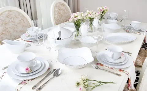 Eleganckie pomysły dekoracja stołu komunijnego: biała zastawa, bukieciki róż, świece i złote zdobienia.