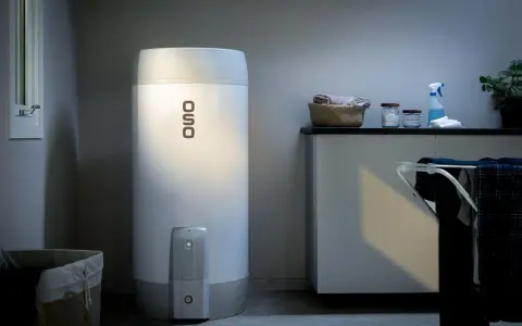 En OSO smart varmvattenberedare står i ett tvättstuga. Bredvid finns en tvättkorg och en torkställning med kläder.