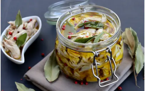 Tonno di coniglio sott'olio, sfilacciato e conservato in un barattolo di vetro con erbe aromatiche e pepe rosa.
