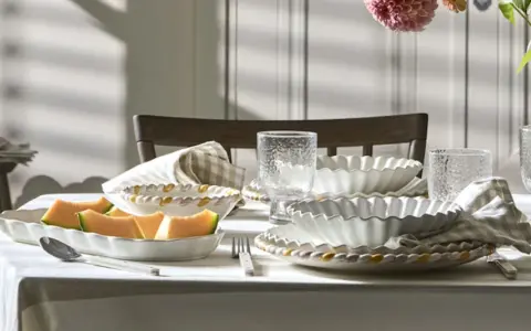 Ett dukat bord med en fin servis, frukt och blommor. Vackra vita skålar med vågiga kanter och glas med textur.