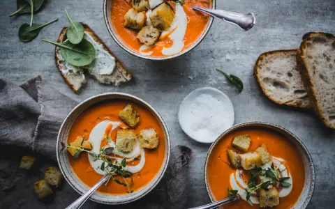 Tre skålar med krämig tomatsoppa, toppad med krutonger och en virvel av grädde. Perfekt för ett mysigt tomatsoppa recept.