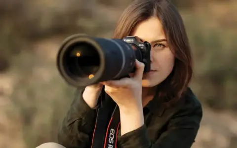 Kobieta z aparatem Canon EOS R7, skupiona na kadrze. Jej oczy błyszczą, a obiektyw sugeruje zaawansowane techniki fotograficzne.