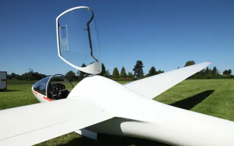 Ein weißer Motorsegler mit geöffneter Haube steht auf einer grünen Wiese.