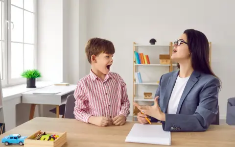 Chłopiec z otwartymi ustami wykonuje ćwiczenia podniebienia miękkiego z logopedą.