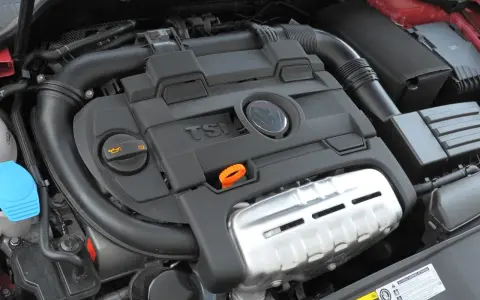 Silnik 1.4 TSI z widocznym logo VW. Widoczne elementy to m.in. pokrywa silnika, przewody, zbiornik płynu i filtr oleju.