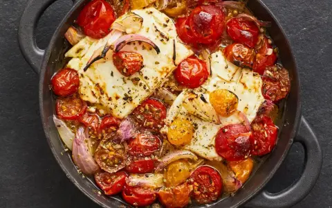 Heißer, gebackener Feta mit Kirschtomaten und roten Zwiebeln in einer Pfanne, mit Kräutern bestreut.