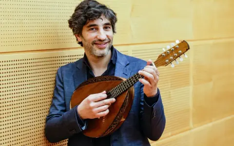 Mann mit Mandoline, die acht Saiten hat, lächelt.