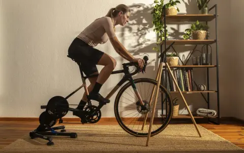 Frau trainiert auf einem Heimtrainer, was ist spinning? Sie tritt kräftig in die Pedale, während im Hintergrund ein Regal mit Pflanzen und Büchern steht.