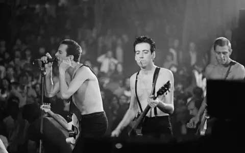 Le chanteur de The Clash, Joe Strummer, chante avec passion devant une foule en délire, guitare à la main.