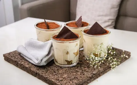 Quatre verrines de tiramisu, garnies de cacao et d'une feuille de chocolat. Une serviette grise et des petites fleurs blanches décorent le plateau en liège. Pourquoi mon tiramisu est liquide ?