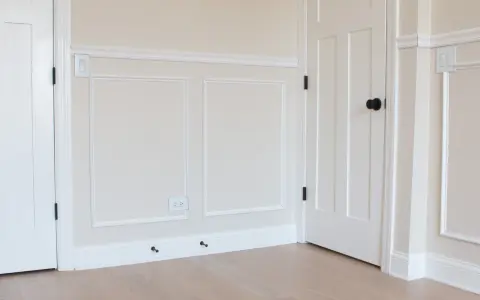 A room with a DIY chair rail, wainscoting, and white doors. The walls are painted a light cream color.