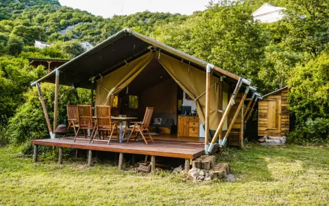 Glamping w Czarnogórze: namiot z drewnianym tarasem, stołem i krzesłami, otoczony zielenią. Idealne miejsce na relaks.
