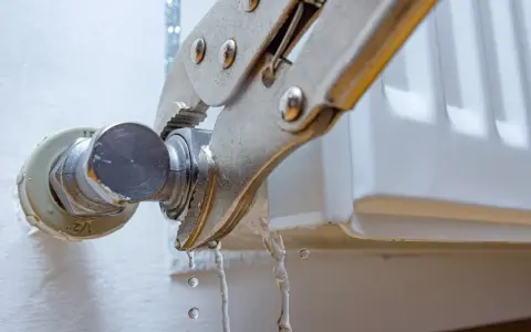 Herramienta sujetando una conexión de radiador mientras gotea agua. Guía visual para como quitar un radiador.