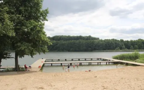 Plaża nad jeziorem Zaleskim z drewnianymi pomostami, na których bawią się ludzie.