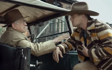 Due uomini in auto discutono animatamente. Uno, al volante, con cappello e giacca chiara, sembra implorare l'altro. Quest'ultimo, con un cappello simile e una giacca a righe, ascolta con espressione tesa, forse coinvolto negli eventi del "killer of the...