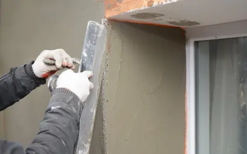 Lavori di intonacatura attorno alle spallette delle finestre, con un operaio che stende il materiale.