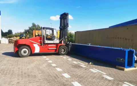 Czerwony wózek widłowy przygotowuje się do przeładunku długiego, niebieskiego elementu. To przykład sprawnego cross dockingu.