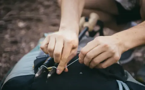 Ręce zapinają kijki trekkingowe do plecaka. Prosty sposób, jak przypiąć kijki do plecaka, by były zawsze pod ręką.