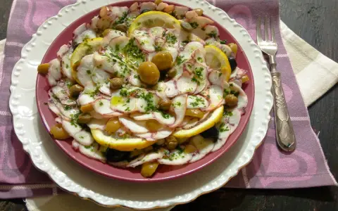 Carpaccio di polpo fresco, guarnito con olive, capperi e fette di limone, un piatto estivo da gustare.