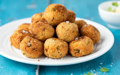 Pile di polpette tonno e ricotta dorate e croccanti, cosparse di sale grosso, su un piatto bianco.