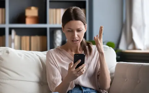 Zirytowana kobieta próbuje włączyć internet w telefonie, gestykulując z frustracją.