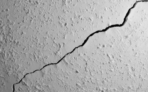 Gros plan sur une fissure traversant un plafond texturé. La fissure est sombre et profonde, contrastant avec la surface blanche et irrégulière.