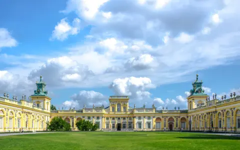 Pałac w Wilanowie zachwyca architekturą i ogrodami. Można zobaczyć bogato zdobione fasady, wieże i zielone trawniki.
