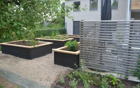 Snygga svarta odlingslådor med träkant ger inspiration för en modern trädgård. Planteringar med grönska och en träskärm.