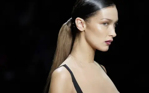 Bella Hadid luce un elegante peinado de cola de caballo con pelo efecto mojado, resaltando su perfil y maquillaje.