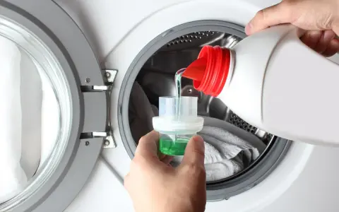 Versando detersivo liquido in un misurino per il prelavaggio lavatrice.