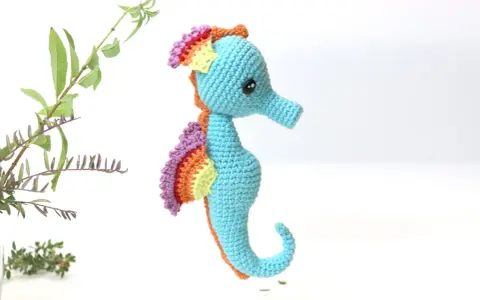Caballito de mar amigurumi patron gratis. Un adorable caballito de mar tejido a crochet, con aletas arcoíris y cuerpo azul, listo para navegar en tu imaginación.