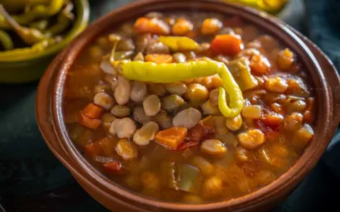 Un cuenco de barro con pochas a la navarra, un guiso reconfortante de alubias blancas, verduras y un pimiento verde.
