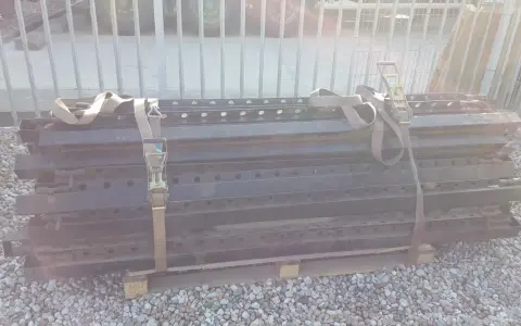 Stos czarnych, metalowych elementów naczepy z pasami transportowymi.