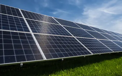 Reihen von Solarmodulen auf einer grünen Wiese unter blauem Himmel. Erneuerbare Energie durch Solarenergie.