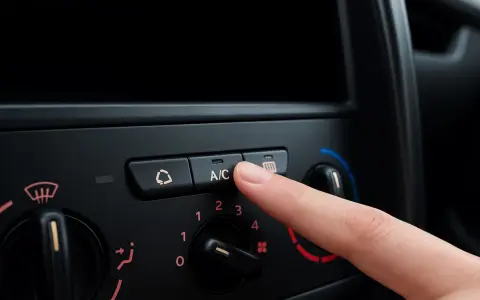 Finger presses the A/C button on a car's climate control panel, ready to activate the car air conditioning for a cool ride.