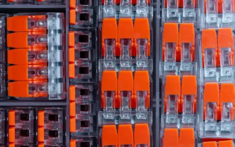 Zbliżenie na pomarańczowe złącza elektryczne w przezroczystych obudowach, ułożone w rzędy.
