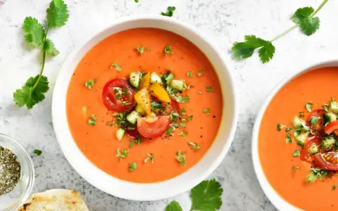 Två skålar med uppfriskande gazpacho, toppad med färska grönsaker. Ett perfekt gazpacho recept för varma dagar.