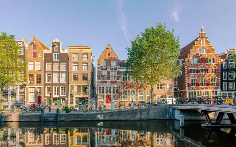 Bunte Grachtenhäuser spiegeln sich im Wasser. Fahrräder säumen den Kanal. So viel **was kann man in Amsterdam machen**!