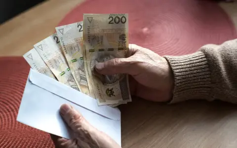 Dłoń trzyma kopertę z banknotami 200 zł. Czy to pieniądze na 800 plus do jakiegoś wieku?