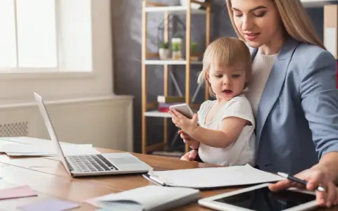 Praca na urlopie macierzyńskim? Młoda mama z dzieckiem przy biurku z laptopem i tabletem, pokazująca, że można łączyć obowiązki.