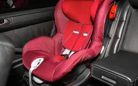 Silla de coche roja en asiento de cuero negro. Las sillas Isofix se pueden poner con cinturón, ofreciendo versatilidad para la seguridad infantil.
