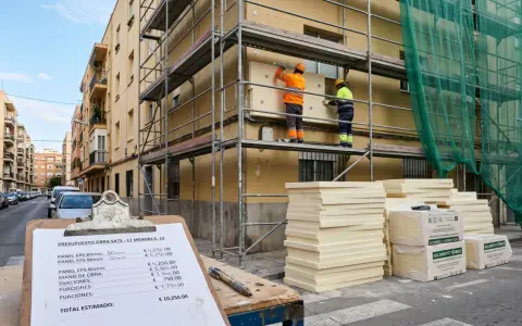 Presupuesto de obra SATE: dos trabajadores instalan aislamiento térmico en fachada. Materiales apilados y presupuesto detallado.