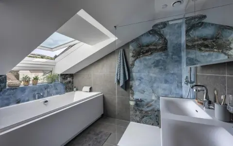 Bagno sottotetto basso con vasca, doccia con piastrelle blu marmorizzate e lucernario.